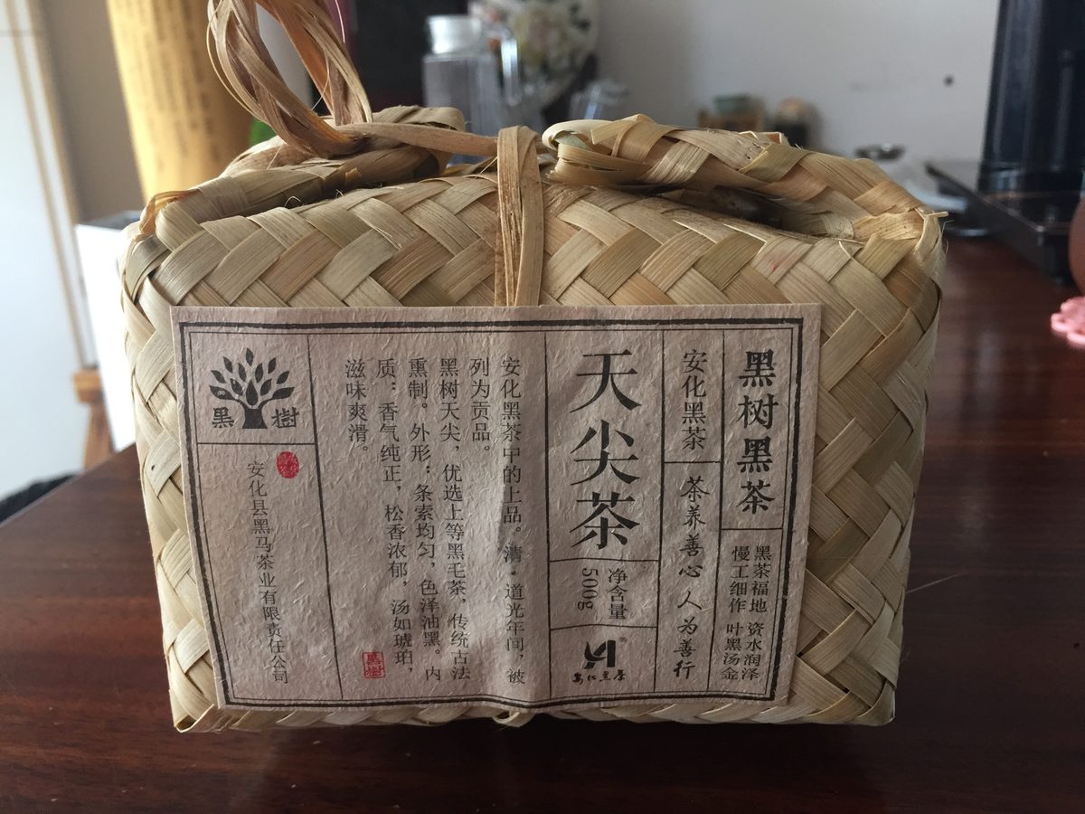 竹编篓装黑茶（天尖茶）置于木质桌面，标签注明产品信息