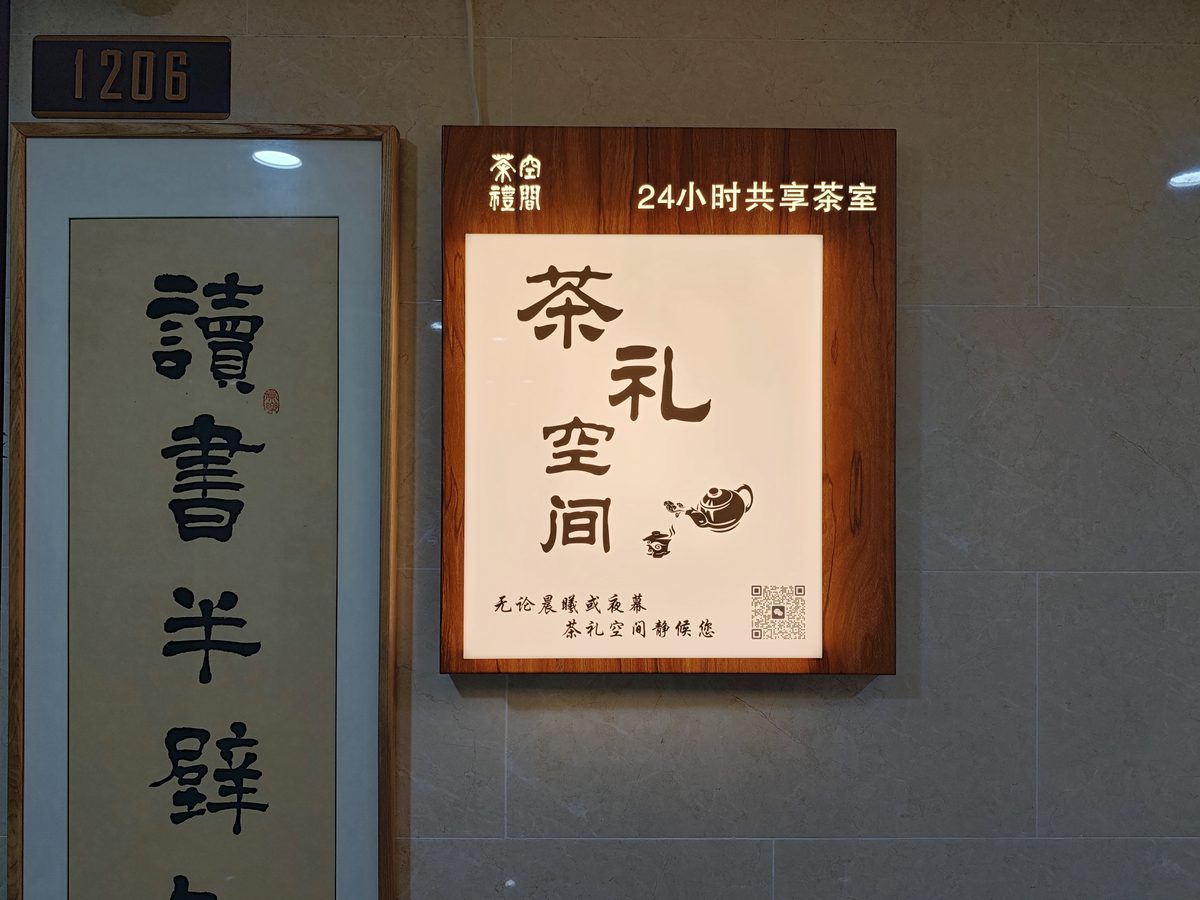 茶礼空间生活馆的共享茶室空间门口，左侧挂书法牌匾，右侧是发光标识牌